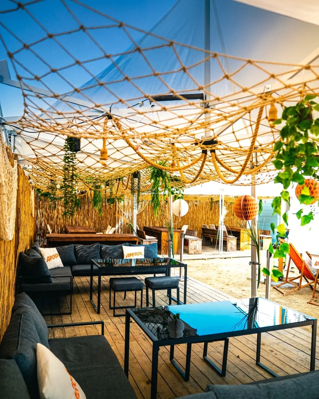 Lounge unter Netzdach mit Sofas und Sandboden